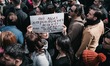 A woman in the crowd holds a powerful cartoon reading: 'No more mothers losing their child...