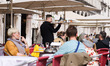 A waiter and tourists at garden cafes in San Marco Square in Venice, Italy on March 14th,...