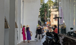 People walk and take photos along a shaded sidewalk near the Saigon Opera House in Ho Chi...