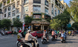 Motorcyclists navigate a busy intersection near an old colonial-style building housing caf...