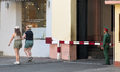 Two foreign visitors pass by a uniformed guard at a restricted entry point near a commerci...
