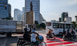 Motorbikes, a truck, and a bus cross a red-striped pedestrian path near a city monument in...