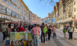 People gather around a charity booth supporting SOS Children's Villages while others walk...