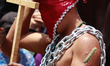A penitent, hooded, carries heavy chains and has thorns buried in the skin, taking part in...