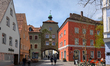 People walk and sit outdoors near the historical archway with the Targobank and pharmacy '...