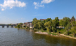 A quiet stretch of the Danube shoreline with residential houses, spring greenery, and a vi...