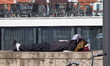 A young woman lies on a stone wall resting in the sun beside a water bottle and bag near a...