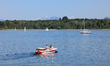 A small motorboat carrying two people moves across the calm waters of Lake Chiemsee as sai...