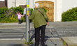An elderly man with walking poles uses a pedestrian crossing while a woman and child wait...