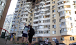 People stand outside an apartment block in the Solomianskyi district damaged by an overnig...
