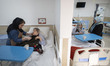 An Iranian woman stands beside her relative's bed as another elderly woman receives care f...