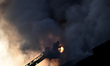 A firefighter in the cradle at the end of a turntable ladder puts out a fire in a building...