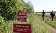 Two men walk along a dirt road past warning signs during a humanitarian demining mission i...