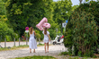 Two women in white dresses hold a large pink balloon shaped as the letter ''B'' near a par...