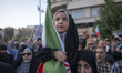 A veiled young Iranian girl holds a country flag during a protest to condemn the U.S. atta...