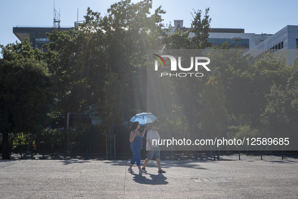 People cover from the sun with an umbrella in Lisbon, Portugal, on July 26, 2025. The area, built for Expo '98, features wide promenades, ga...