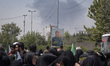 Veiled Iranian women gather beneath a banner featuring a portrait of the former commander...