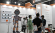 Attendees look at a display featuring a robot mascot at the Robotspace booth during the Au...