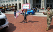 A protestor holds a sign and waves a flag as National Guard troops park vehicles outside o...