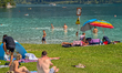 People relax under umbrellas and swim at Lake Plansee during summer in Plansee, Reutte, Ty...