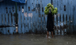 A man carries bananas on his head as he wades through a flooded street with umbrellas duri...