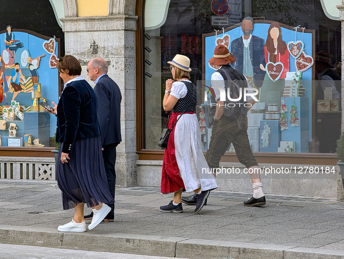 People In Traditional Bavarian Clothing Walking Past Decorated Shop Windows In Munich During Oktoberfest