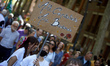 A young woman holds a cardboard sign reading 'All Capitalists Are Bastards'. All trade uni...