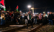 A female protester on the railway tracks leads chants with a megaphone while others illumi...