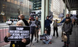 Protesters hold signs and read aloud testimony from Jeffrey Epstein's victims in front of...