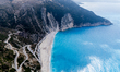 A drone view of Myrtos Beach and the winding coastal road descending to the shoreline on t...