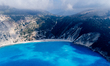 A drone view of Myrtos Beach and the winding coastal road descending to the shoreline on t...