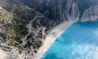 A drone view of Myrtos Beach and the winding coastal road descending to the shoreline on t...