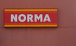 The illuminated logo of the discount supermarket chain Norma is visible on a store facade...