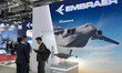 Military officials and visitors from various countries tour the Embraer booth during the S...