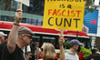 A woman holds a sign saying 'Tommy Robinson is a Fascist Cunt' as a small group of counter...