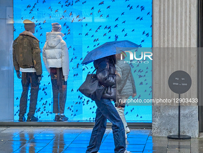 Shoppers With Umbrellas Pass Fashion Storefront On Rainy Day