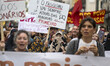 Several women wearing burkas and activists holding protest signs and shouting slogans marc...