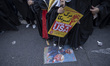 Female Iranian protesters stand next to an anti-U.S. poster depicting the portraits of U.S...