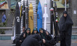 Veiled Iranian women demonstrate the Victory signs as they sit together under scale models...