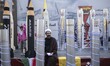 An Iranian cleric and a young girl stand next to scale models of Iran-made ballistic missi...