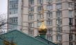The cross crowns the dome of a church as it stands against a contemporary apartment block...