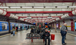 People sit and stand, waiting for a subway train on the platform of Ostbahnhof Metro Stati...