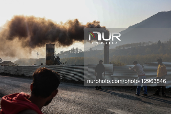 Boys pose for photos near a macadam plant chimney, which emits smoke causing air pollution on the outskirts of Baramulla, Jammu and Kashmir,... by Nasir Kachroo/NurPhoto