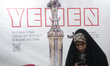 A veiled Iranian woman uses her cell phone while standing in front of a banner as she take...