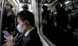 A man wears a face mask as people are reflected in a glass window of a metro train in Toky...