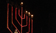 A menorah stands illuminated while people gather during Hanukkah celebrations organized by...