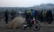 Displaced Palestinians watch as a motorcyclist rides on the sand dunes opposite displaceme...