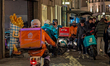 Food delivery couriers from Takeaway.com and Deliveroo stand with motorcycles and thermal...