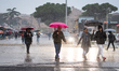 Passengers and pedestrians walk through heavy rain with umbrellas on Piazza dei Cinquecent...