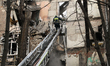 Firefighters extinguish smoldering hotspots amid debris of a multi-storey residential buil...
